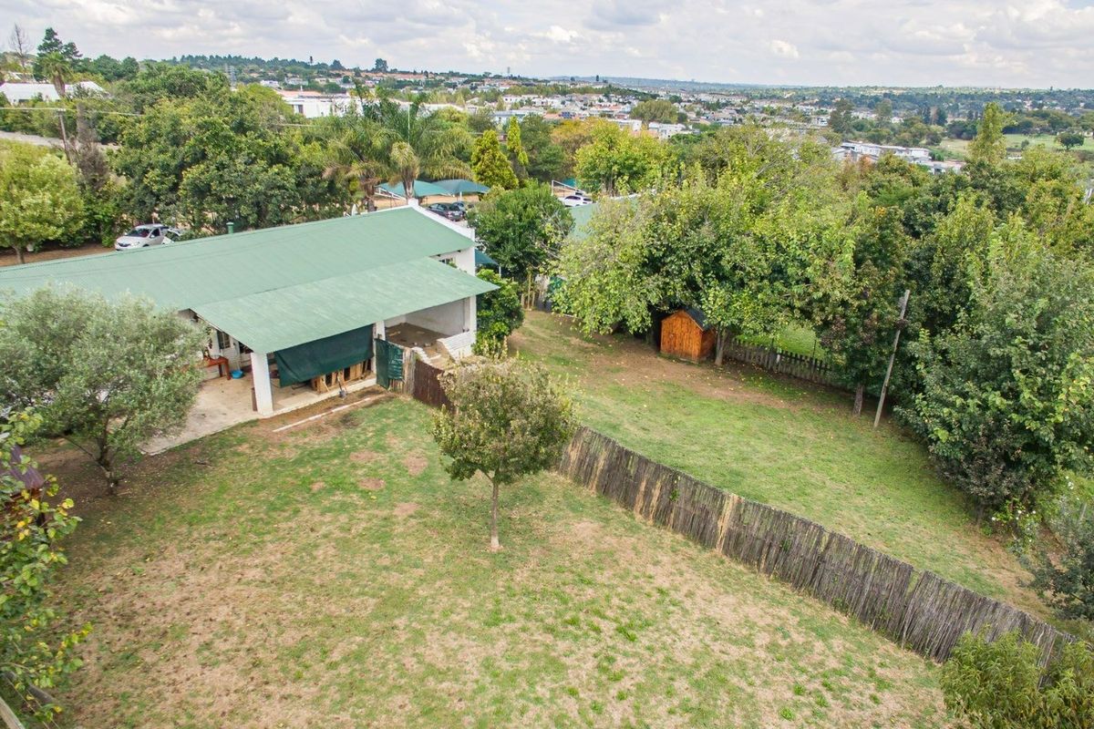 Aerial view of the property grounds featuring a building with a green metal roof, a covered patio area, and a spacious garden with fencing.