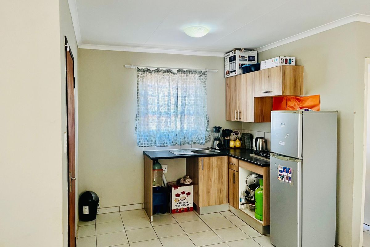 A compact kitchen featuring laminate cabinetry, dark countertops, a stainless steel sink, and neutral ceramic floor tiles.