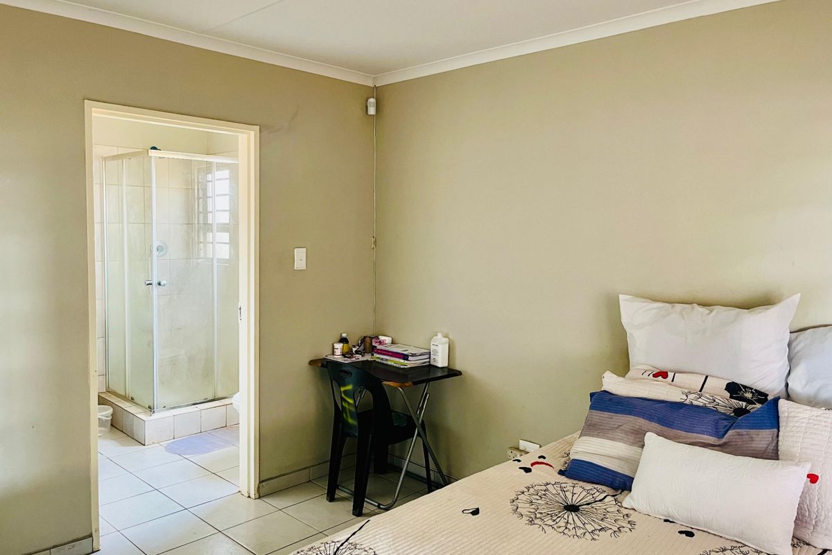 A bedroom featuring neutral wall tones, tiled flooring, and an adjoining en-suite bathroom with a glass-enclosed shower.