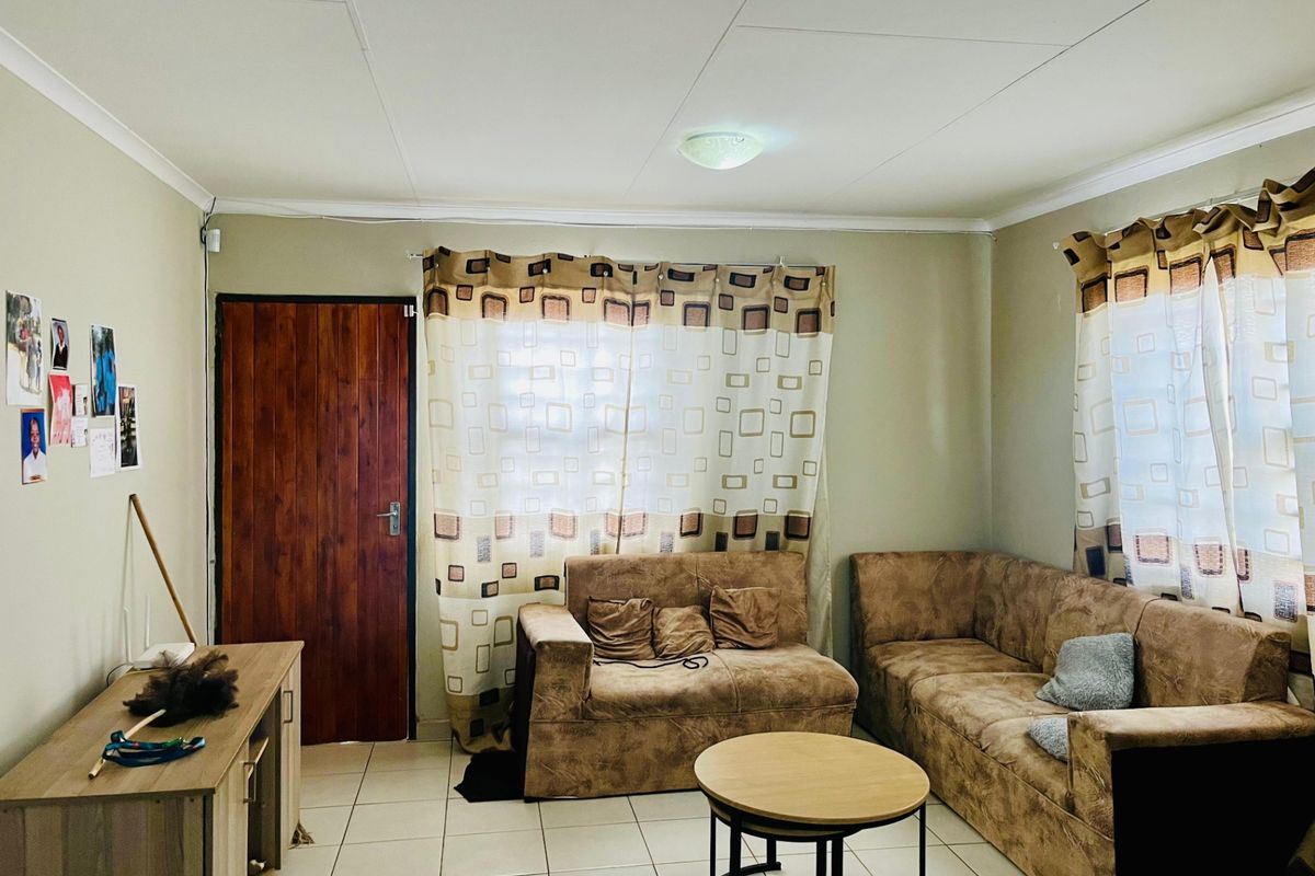A functional living room featuring tiled flooring, a timber entrance door, and neutral wall finishes, providing a comfortable and practical living space.