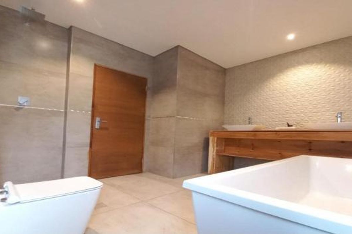 Modern bathroom featuring a double vanity, freestanding bathtub, wall-mounted toilet, and a rain shower head with contemporary tiled finishes.
