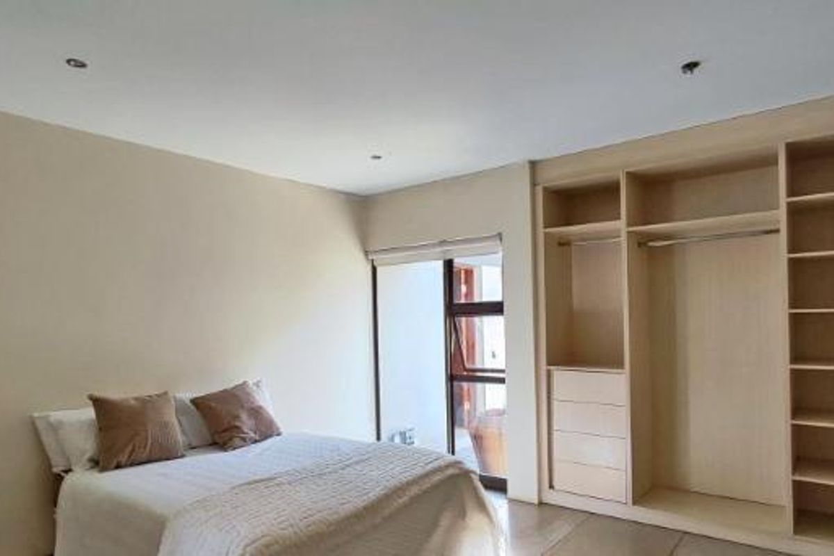 A bright bedroom featuring neutral walls, recessed downlighting, and extensive built-in wooden cabinetry with integrated shelving and hanging space.