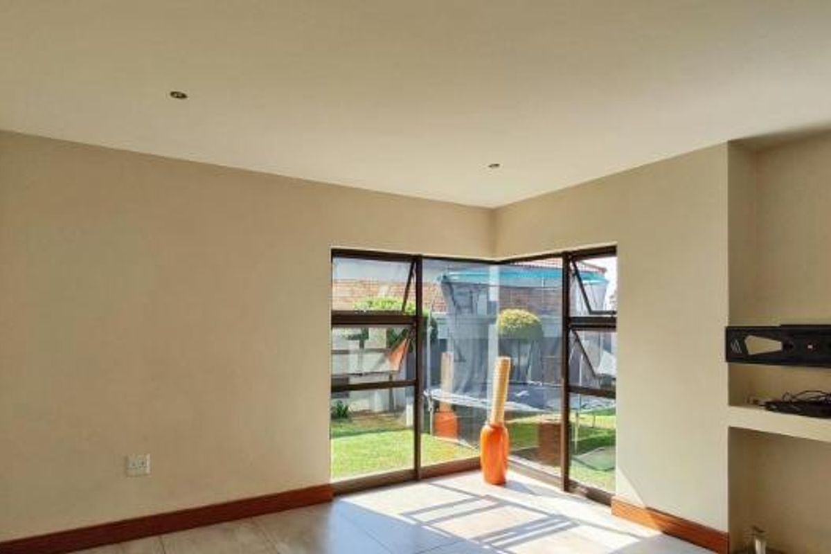 A bright, empty living room featuring tiled flooring, recessed downlights, and a built-in media alcove with views of the rear garden.