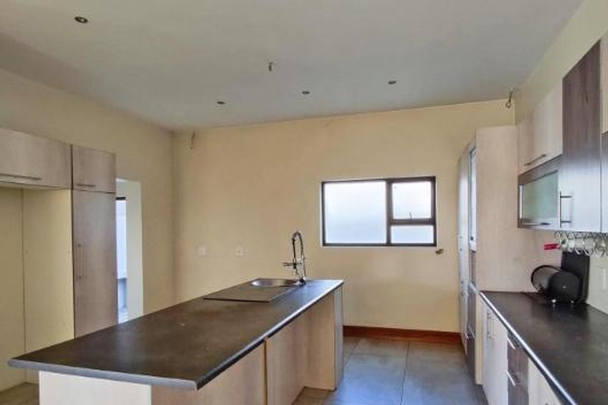 A clean, modern kitchen featuring neutral cabinetry, a central island with a sink, and dark countertops, offering a functional and bright workspace.