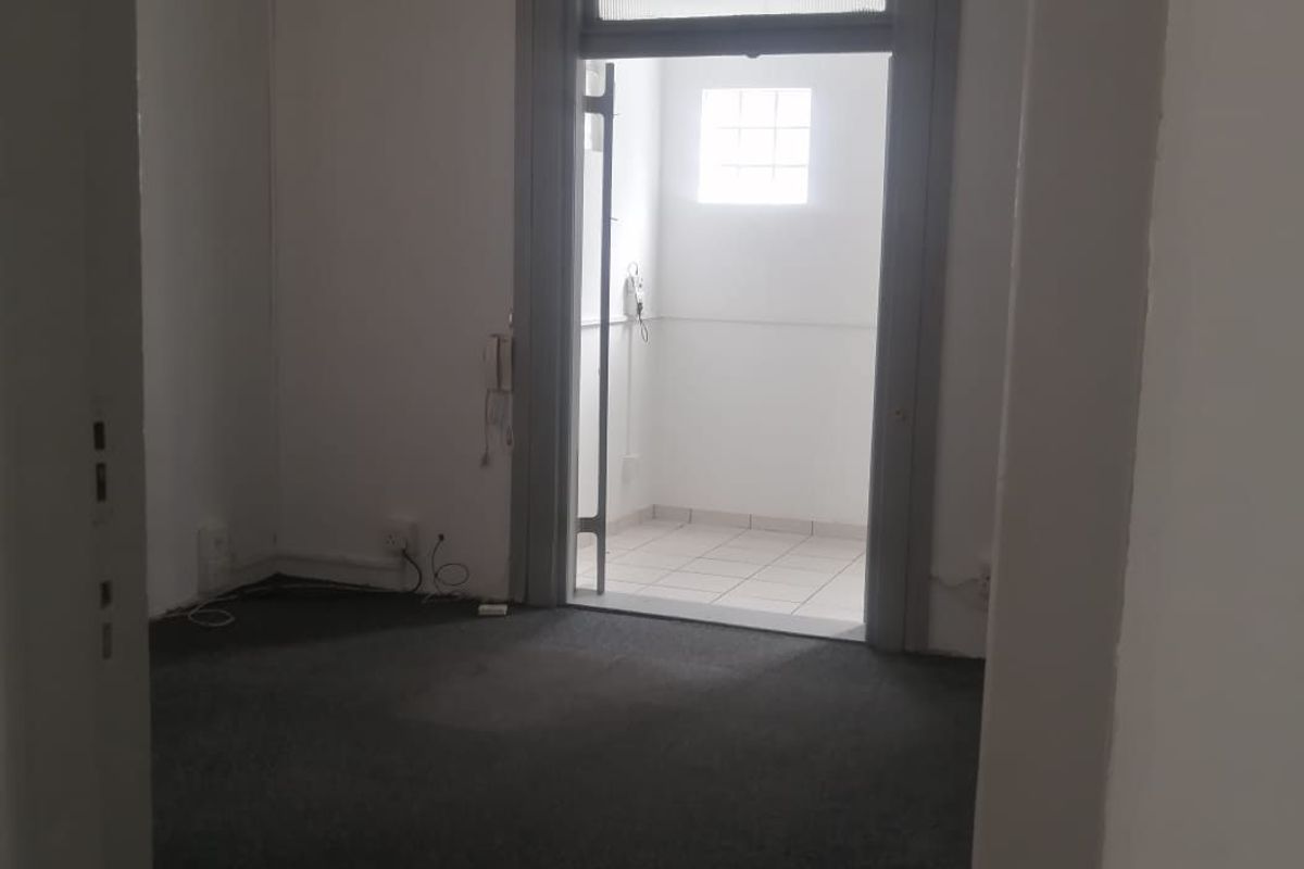 An empty living area featuring carpeted flooring, a wall-mounted air conditioning unit, and a doorway leading to a tiled utility space.