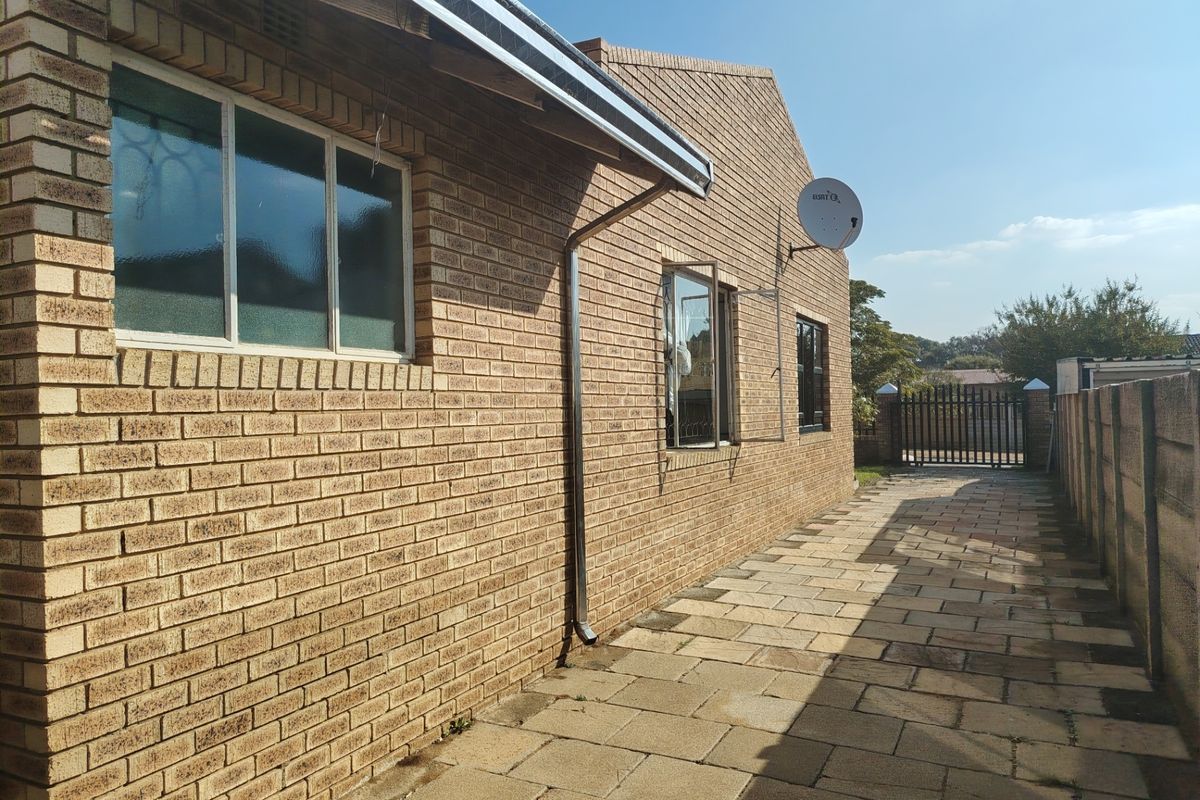 A side view of the house featuring a face brick exterior, paved walkway, and secure boundary wall with a metal gate.