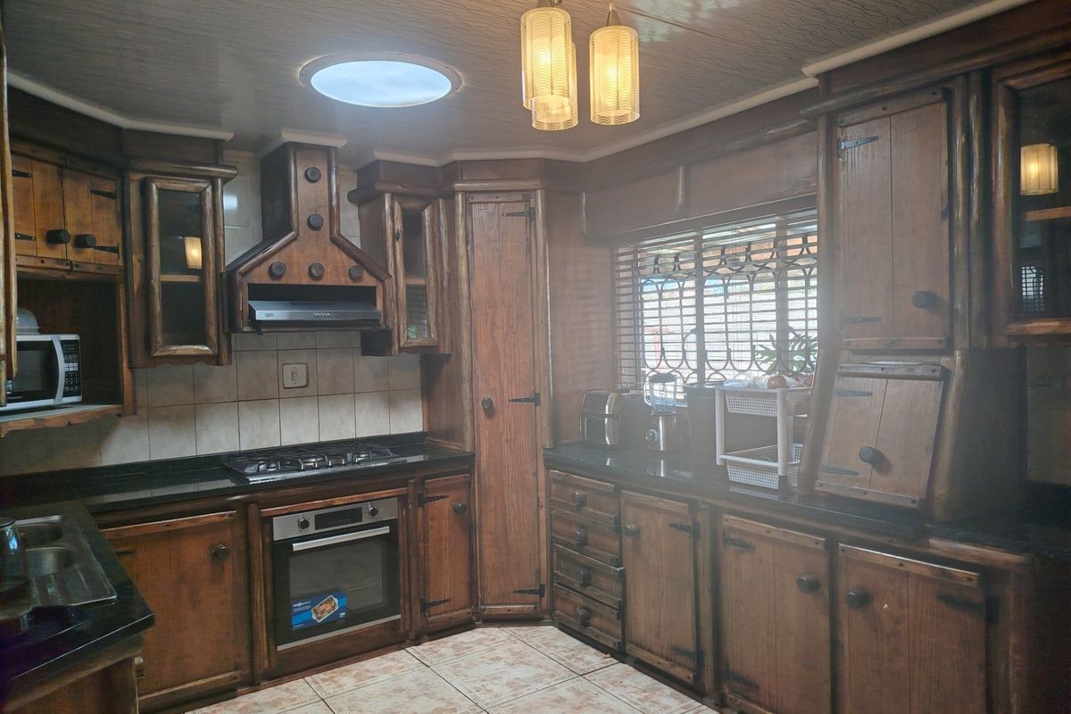 A traditional kitchen featuring dark wood cabinetry, granite countertops, built-in oven and gas hob, complemented by tiled flooring and a functional skylight.