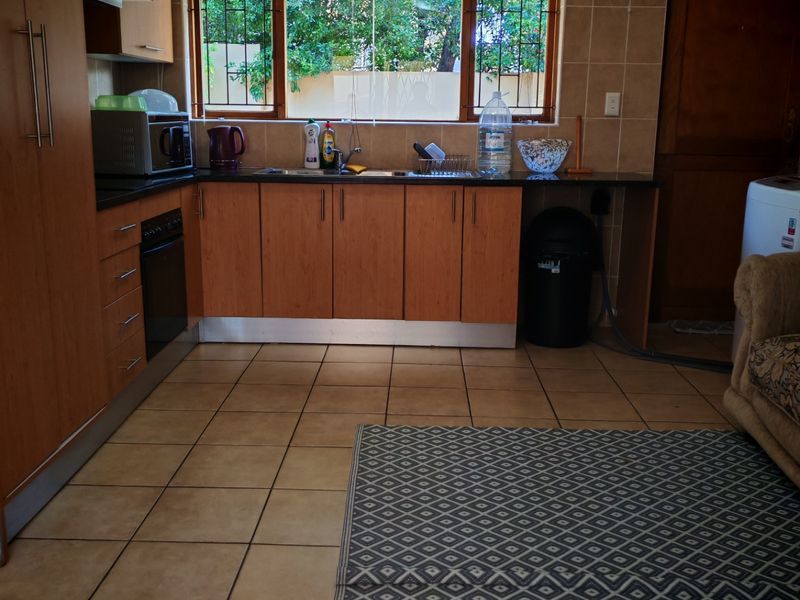A functional kitchen featuring wood-tone cabinetry, tiled flooring, a built-in oven, and a window with security bars overlooking the exterior.