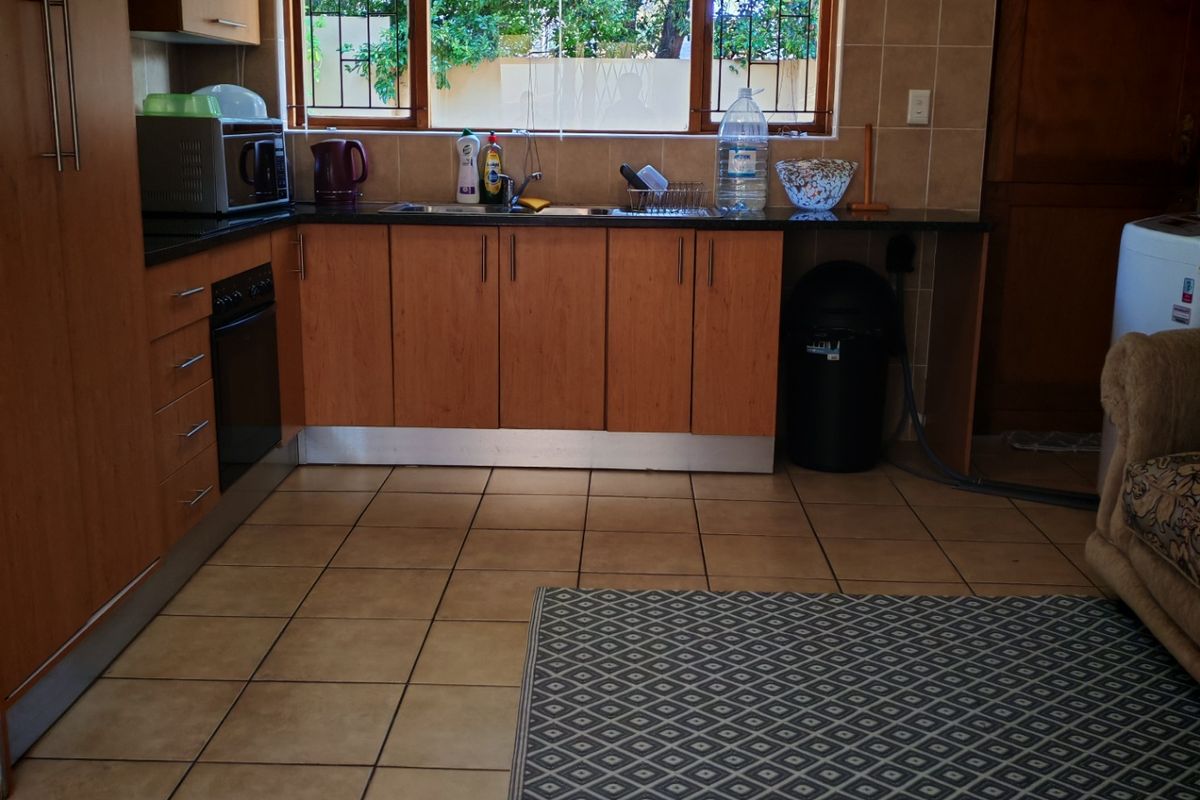 A functional kitchen featuring wood-tone cabinetry, tiled flooring, a built-in oven, and a window with security bars overlooking the exterior.
