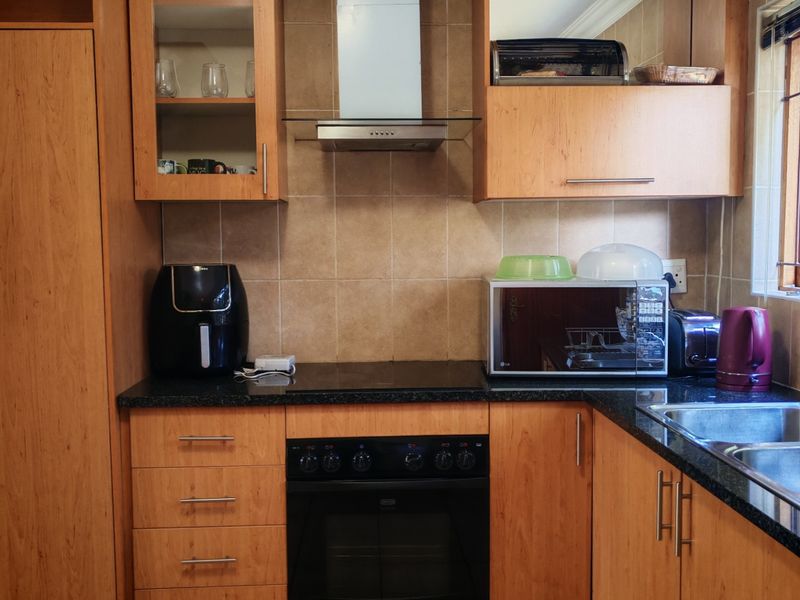 A functional kitchen featuring wood-finish cabinetry, granite countertops, a built-in oven with extractor fan, and tiled flooring.