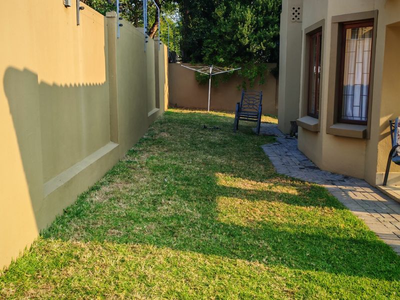 A private rear garden area featuring a well-maintained lawn, paved walkway, and secure perimeter wall with electric fencing.
