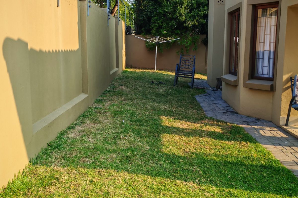 A private rear garden area featuring a well-maintained lawn, paved walkway, and secure perimeter wall with electric fencing.