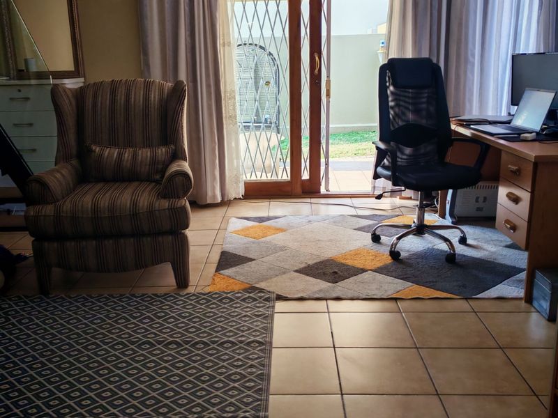 A living area featuring ceramic floor tiles and a sliding glass door with a security gate, providing direct access to the outdoor patio.