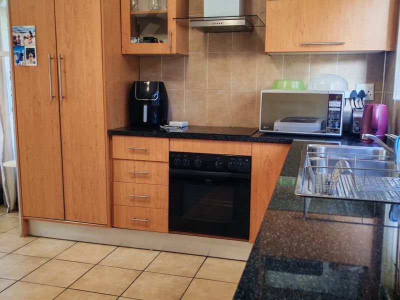 A functional kitchen featuring wood-finish cabinetry, granite countertops, integrated oven and hob, and tiled flooring with a neutral backsplash.