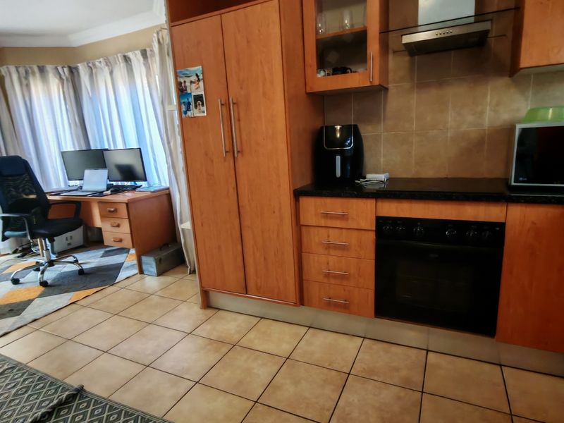 Open-plan kitchen area featuring wood-finish cabinetry, built-in oven, extractor fan, and tiled flooring, seamlessly flowing into a workspace area.