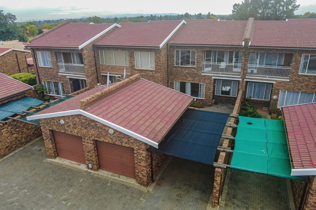 Aerial view of a face-brick townhouse complex featuring double garages, carports, and upper-level balconies with tiled roofing.