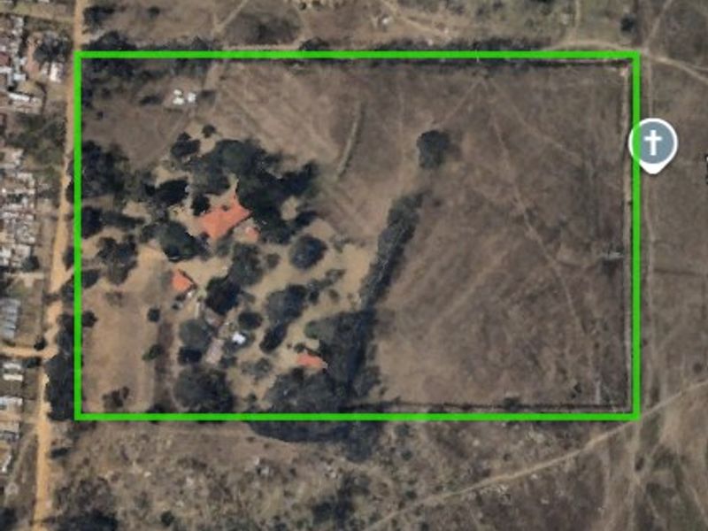 Aerial view of a large farm property with a fenced perimeter, multiple structures, and established trees on the land.