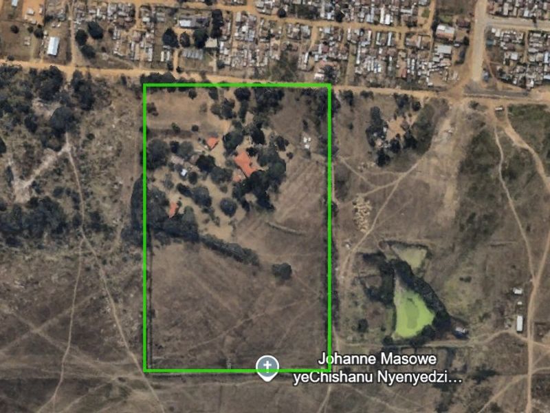 Aerial view of a large farm property featuring multiple structures, mature trees, and a clearly defined fenced boundary within a rural landscape.
