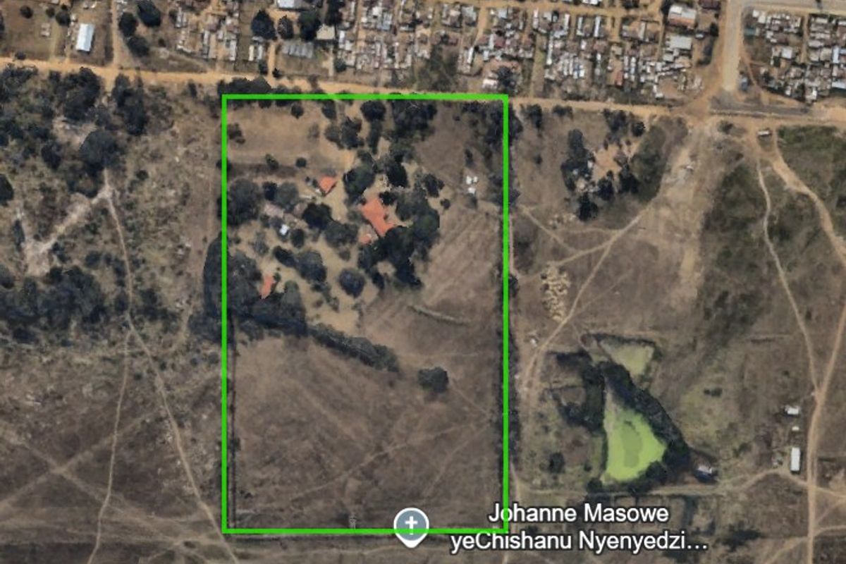 Aerial view of a large farm property featuring multiple structures, mature trees, and a clearly defined fenced boundary within a rural landscape.