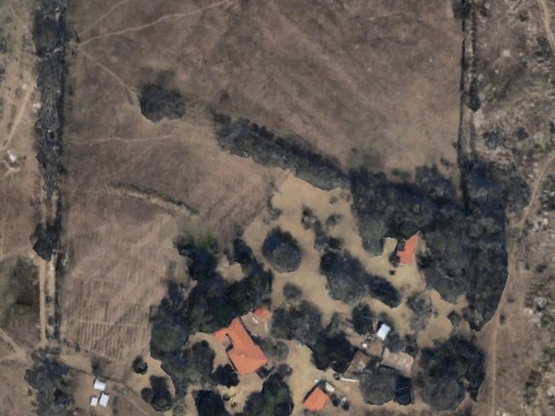 Aerial view of a large farm property featuring a main dwelling, several outbuildings, and a fenced perimeter surrounded by open land and mature trees.