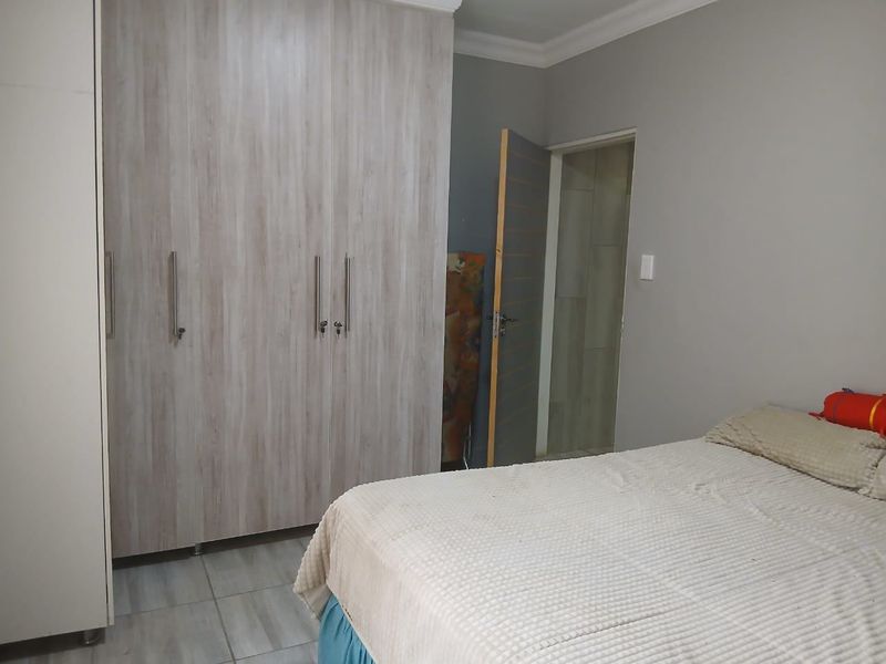 A bedroom featuring built-in wooden wardrobes and tiled flooring, with an adjacent doorway leading to an en-suite bathroom.