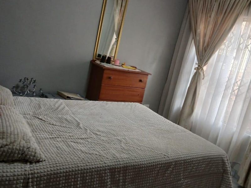 A comfortable bedroom featuring tiled flooring, neutral wall tones, and a window dressed with curtains, providing a functional and well-lit sleeping space.