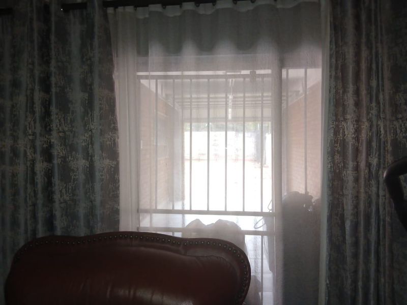 View from an interior space looking out through a window with security bars towards an exterior paved area.