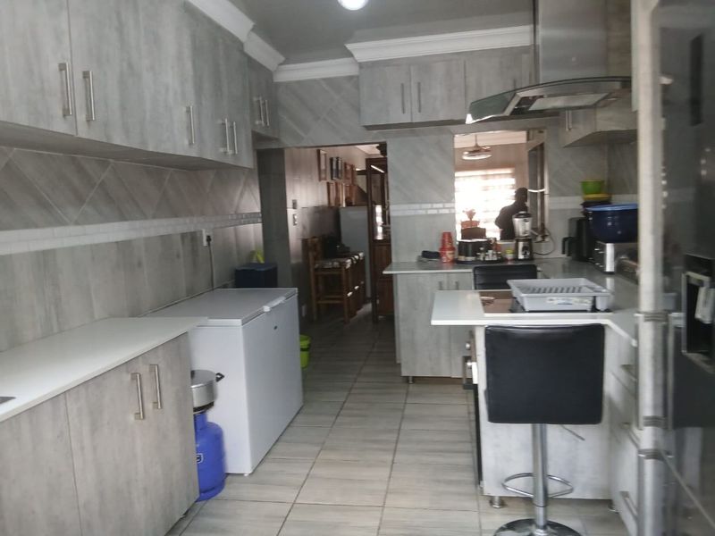 A functional kitchen featuring light wood-grain cabinetry, tiled splashbacks, and a breakfast bar area with integrated extractor fan.