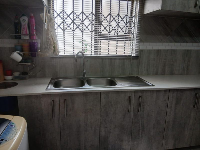A functional kitchen area featuring a double stainless steel sink, modern grey wood-look cabinetry, and a security gate over the window.