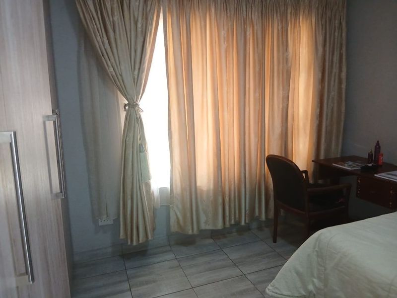A bedroom featuring tiled flooring and built-in cabinetry, illuminated by natural light through large window curtains.