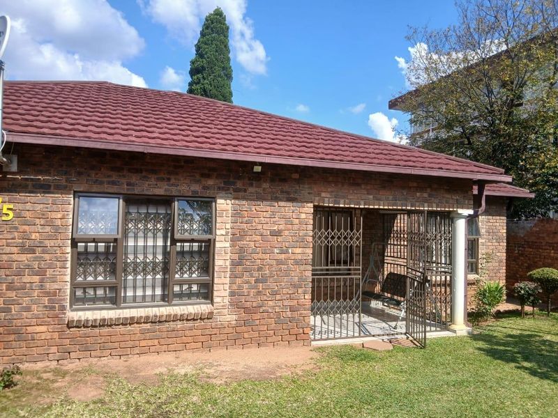 A view of the exterior rear of the brick house, featuring a covered patio area with security gates and a small garden.