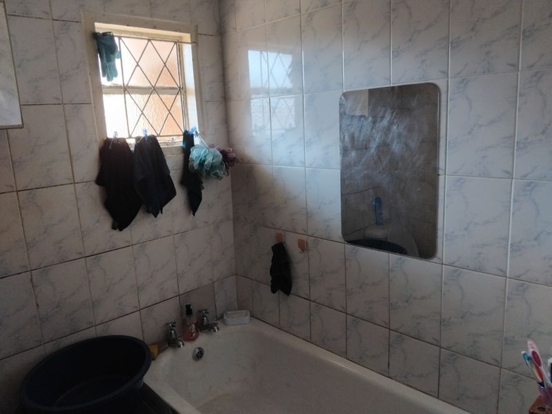 A dated bathroom featuring a standard bathtub, tiled walls, and a window with security bars, offering potential for a modern renovation.