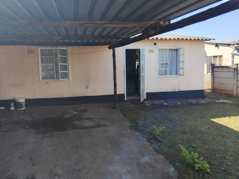 Rear exterior view of the house featuring a covered patio area, security bars on windows, and a fenced yard with concrete paving.