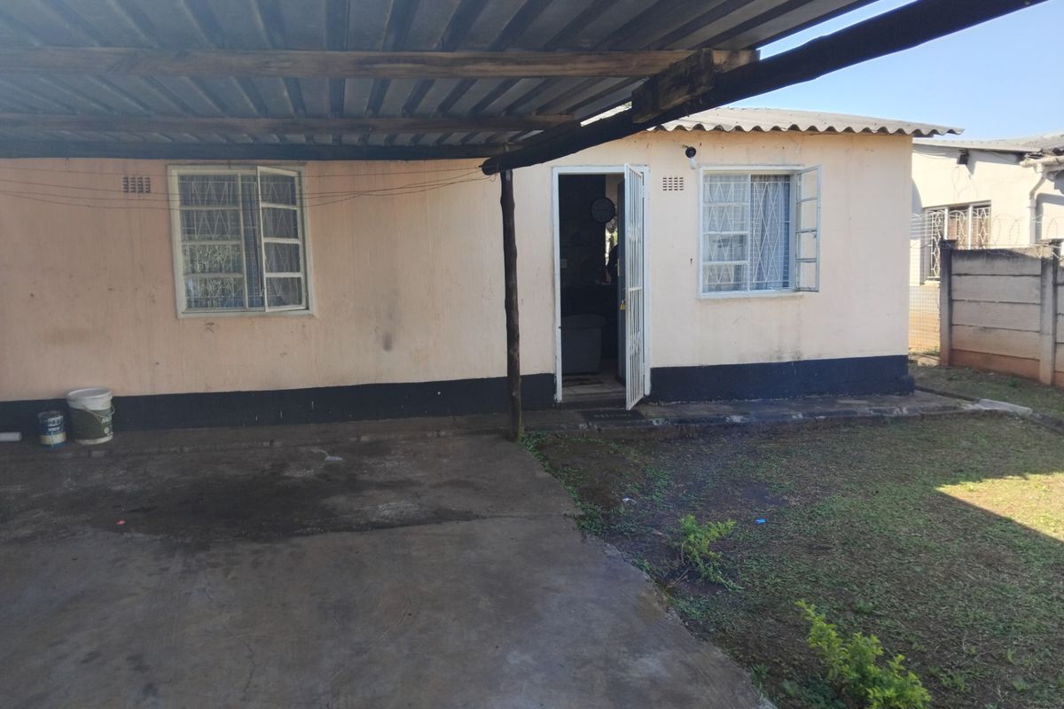 Rear exterior view of the house featuring a covered patio area, security bars on windows, and a fenced yard with concrete paving.