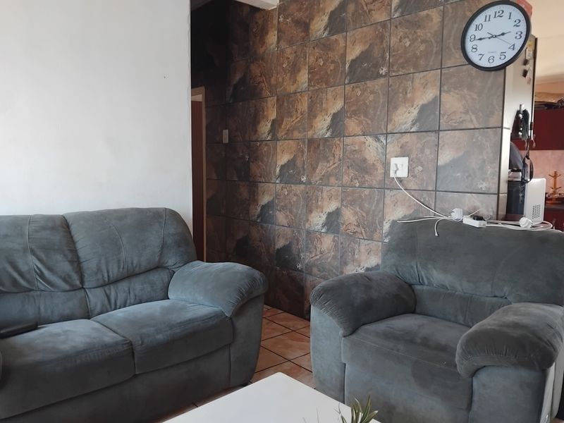 Living room area featuring a prominent tiled feature wall and ceramic floor tiles, offering a dated aesthetic ready for modernization.