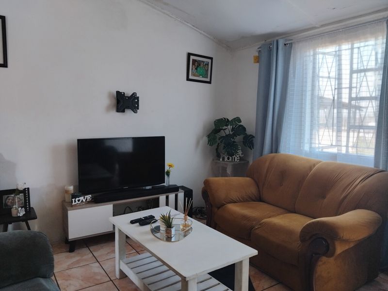 A living room featuring tiled flooring and a window with security bars. The ceiling shows signs of wear and requires maintenance.