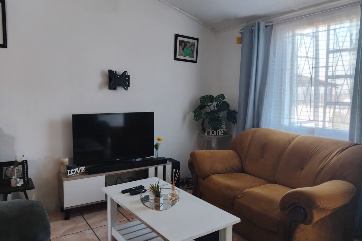 A living room featuring tiled flooring and a window with security bars. The ceiling shows signs of wear and requires maintenance.