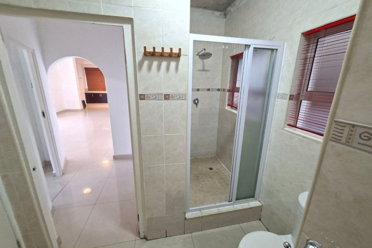 A functional bathroom featuring a shower enclosure, toilet, and tiled finishes. The space shows signs of wear and requires maintenance on the ceiling.