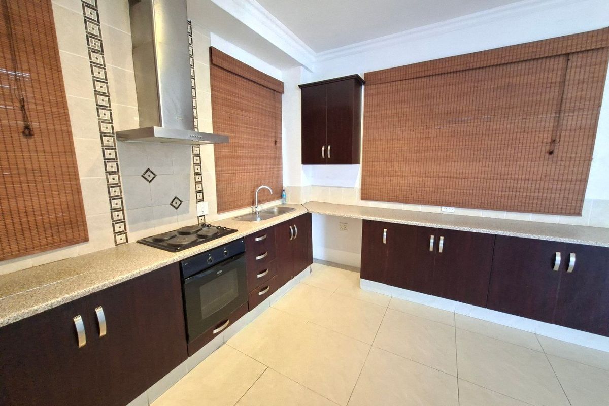 A functional kitchen featuring dark wood cabinetry, granite countertops, built-in oven, hob, extractor fan, and tiled flooring.