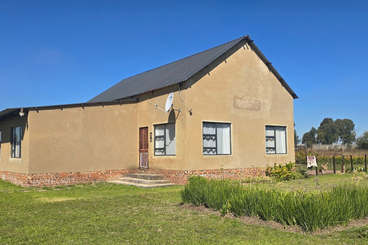 Rear view of a farm-style dwelling featuring a metal roof, brick foundation, and established garden surroundings.