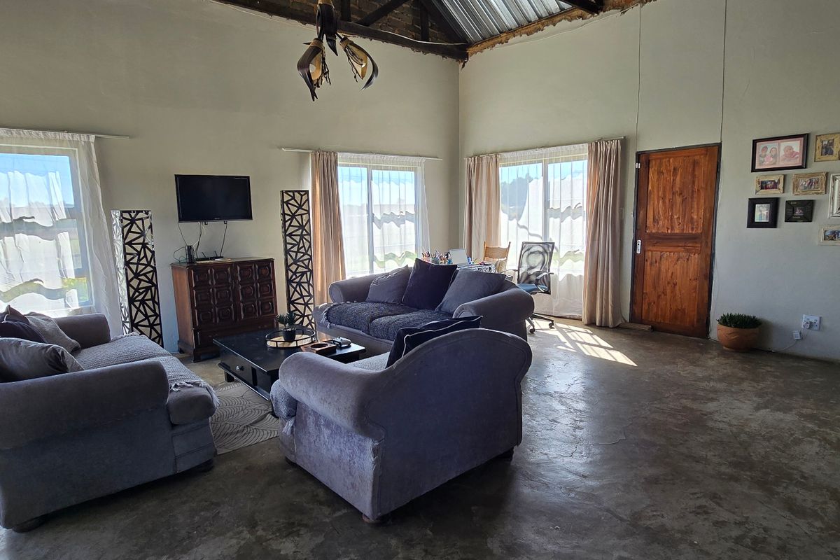 Spacious living area featuring high ceilings with exposed timber trusses, polished concrete floors, and large windows providing ample natural light.