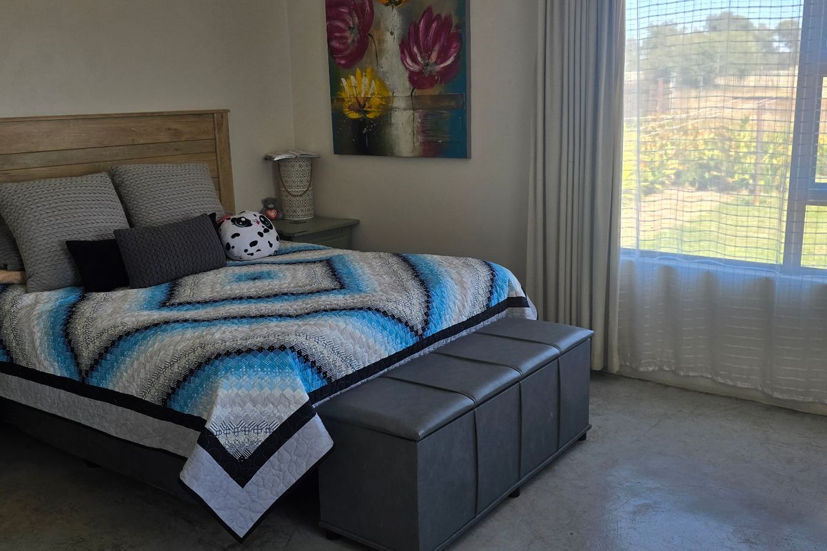 A well-lit bedroom featuring polished concrete flooring and a large window with curtain tracks, offering a view of the exterior garden area.