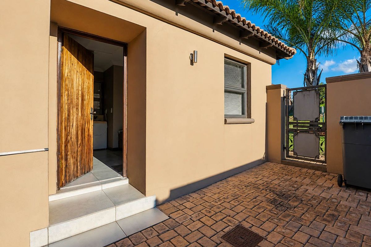 A well-maintained rear exterior area featuring a paved patio, secure wrought iron gate, and direct access to the interior through a timber door.