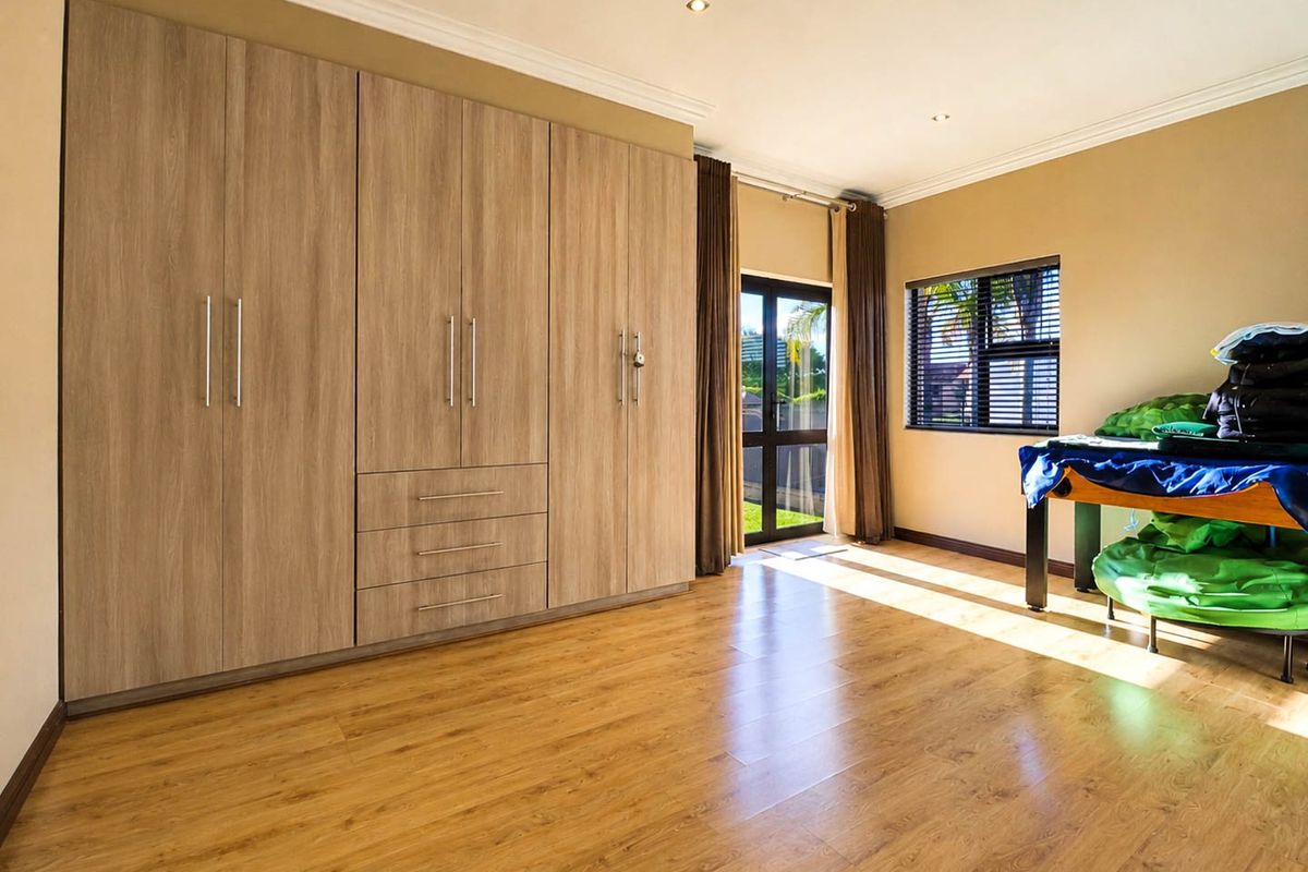 Spacious bedroom featuring extensive built-in cabinetry, warm laminate flooring, and direct access to the garden through a sliding glass door.