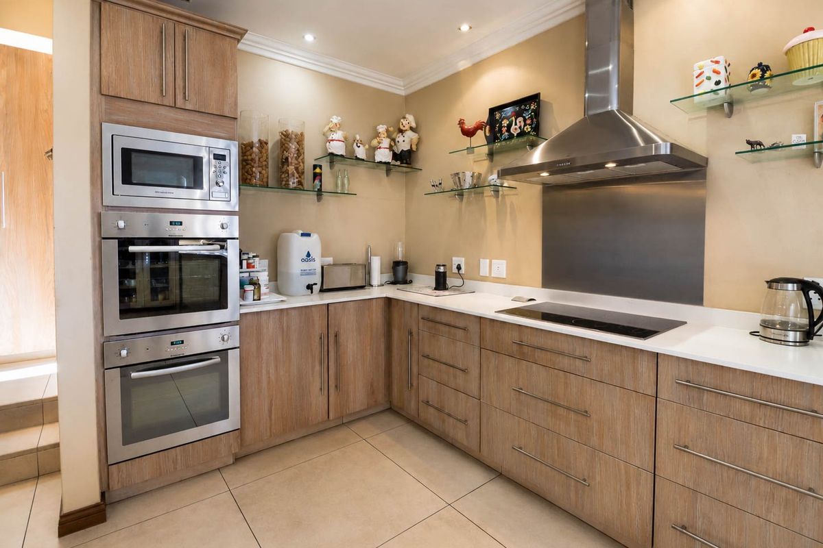 Modern kitchen featuring wood-finish cabinetry, stone countertops, stainless steel appliances including a built-in oven, microwave, and extractor fan, with tiled flooring.