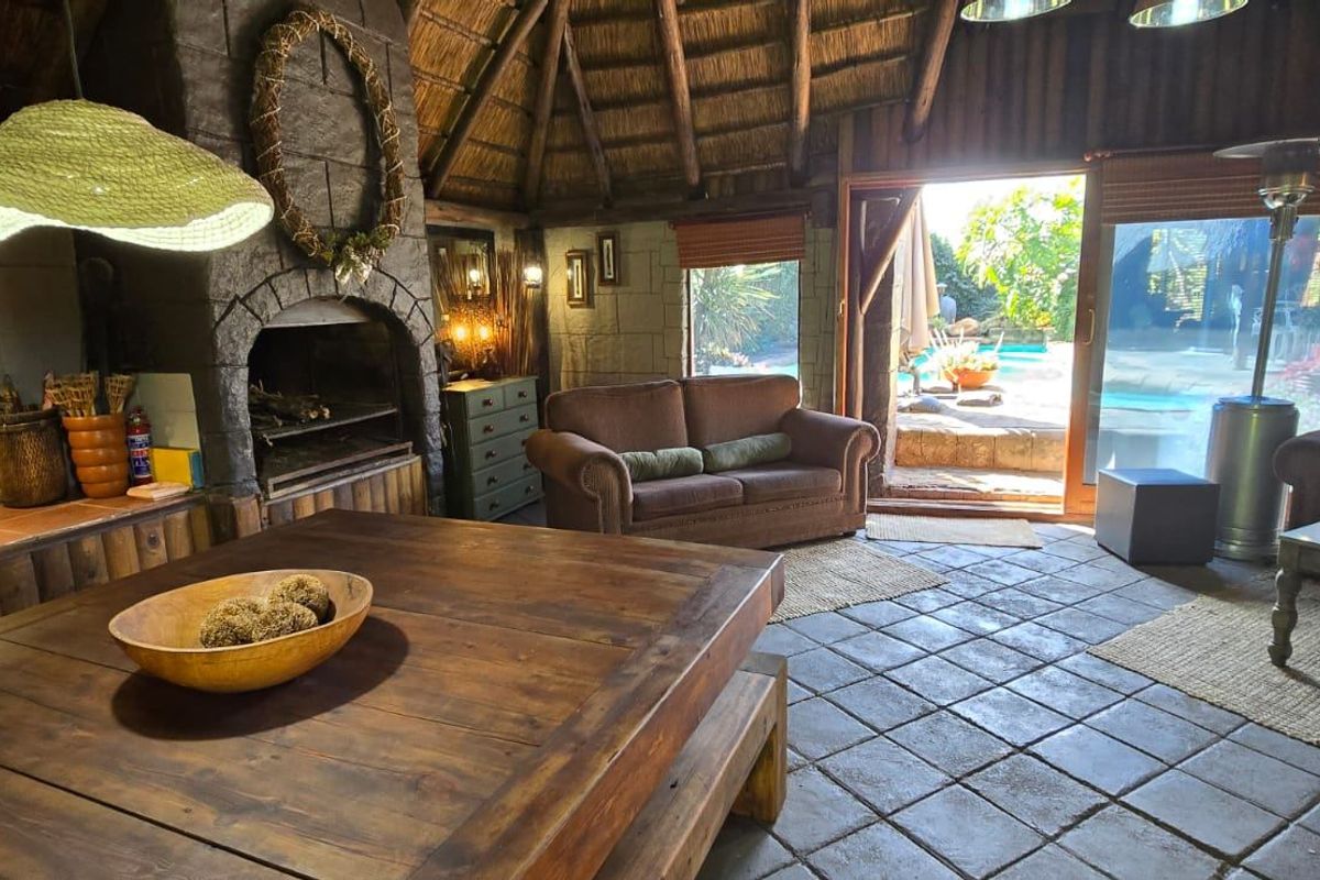 Rustic living area featuring a traditional thatched roof, stone fireplace, and tiled flooring, with direct access to the outdoor pool area.