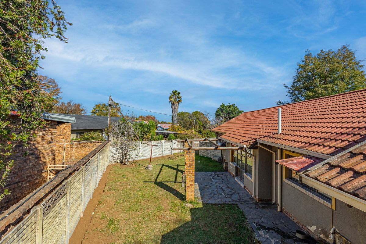Rear view of the property featuring a tiled roof, stone paved patio area, brick pergola, and a private garden enclosed by boundary walls.