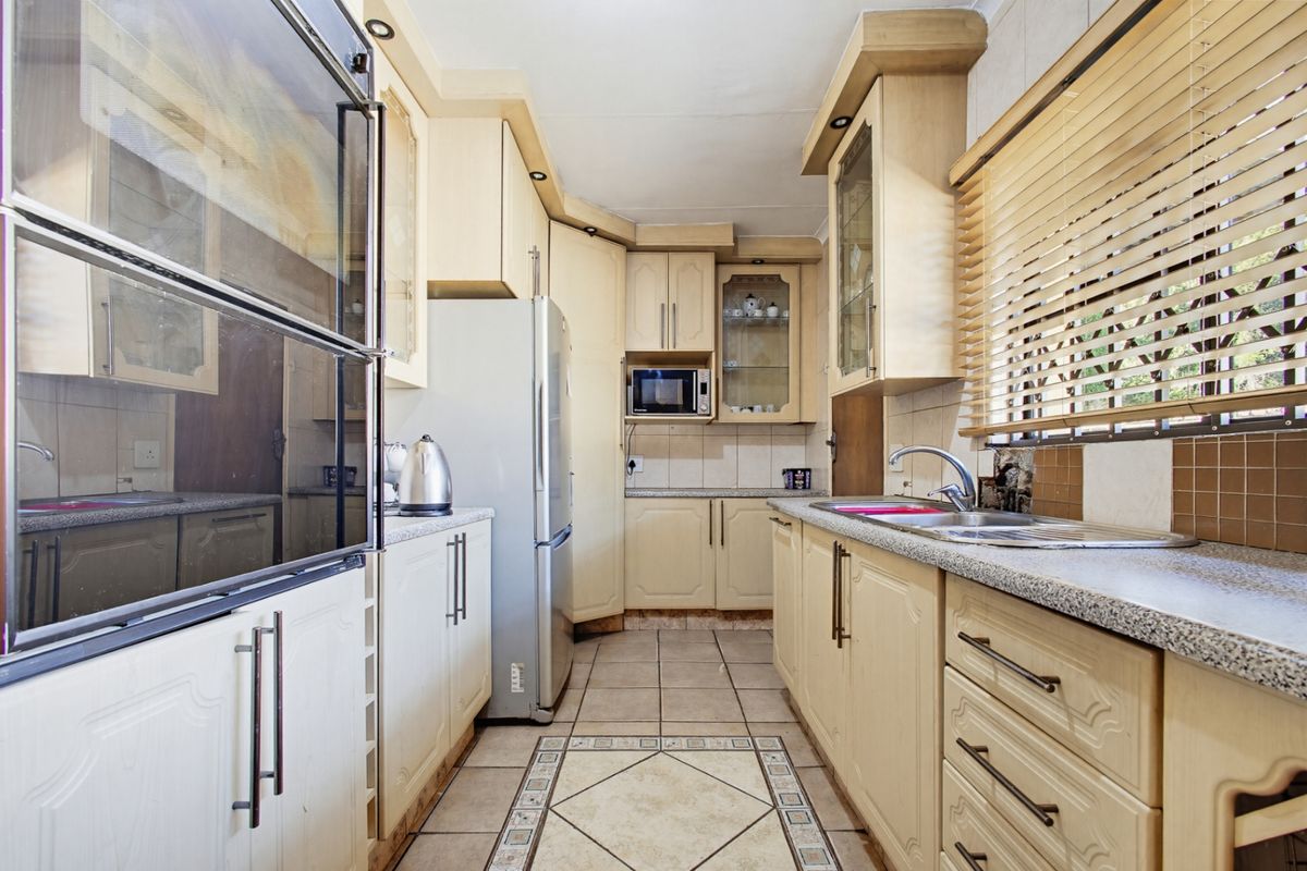 A functional kitchen featuring light-toned cabinetry, laminate countertops, a double stainless steel sink, and tiled flooring with a decorative inlay.