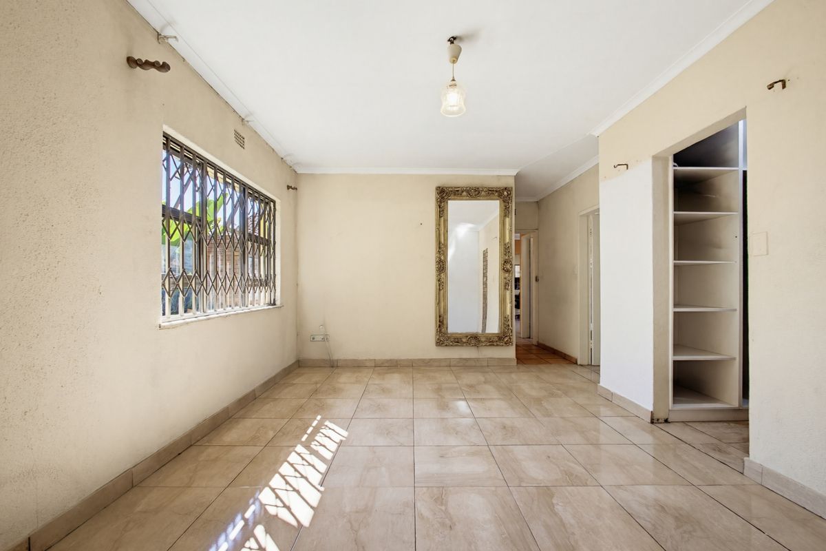 An empty living room featuring tiled flooring, a security gate on the window, and built-in shelving, requiring minor cosmetic updates.