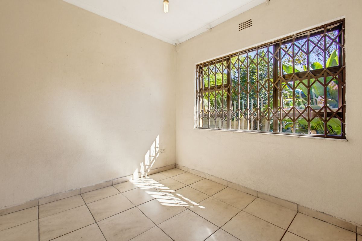 An empty bedroom featuring tiled flooring and a window fitted with a security gate, offering a blank canvas for potential interior design updates.